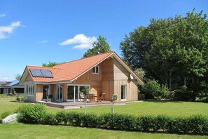 Ein zweistöckiges Haus mit geneigtem Dach, einer überdachten Terrasse und einem gepflegten Rasen.