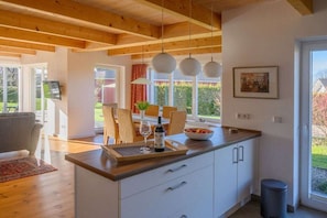 Eine moderne Küche mit Holzbalken, einem Essbereich mit Tisch und Stühlen und einem Ausblick durch das Fenster.