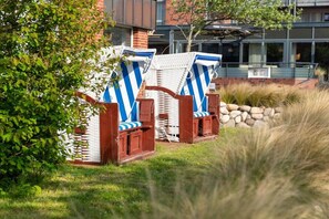 Outdoor wicker lounge chairs with blue and white stripes, a brick building, and a grassy area. - Apartment in Juist with swimming pool (Juist)