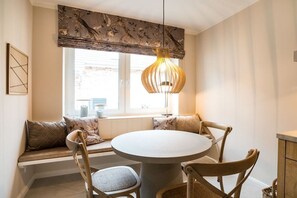 A dining area with a round table, four chairs, a hanging light fixture, and a window with a view. - Holiday apartment with 2 bedrooms (Fehmarn)