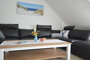 Ein modernes Wohnzimmer mit einer schwarzen Ledersofa, einem weißen Couchtisch und einem Gemälde einer Strandlandschaft an der Wand.
