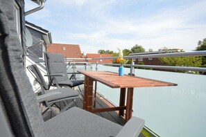 Eine Terrasse mit Tisch und Stühlen, mit Blick auf ein Gewässer und Gebäude.