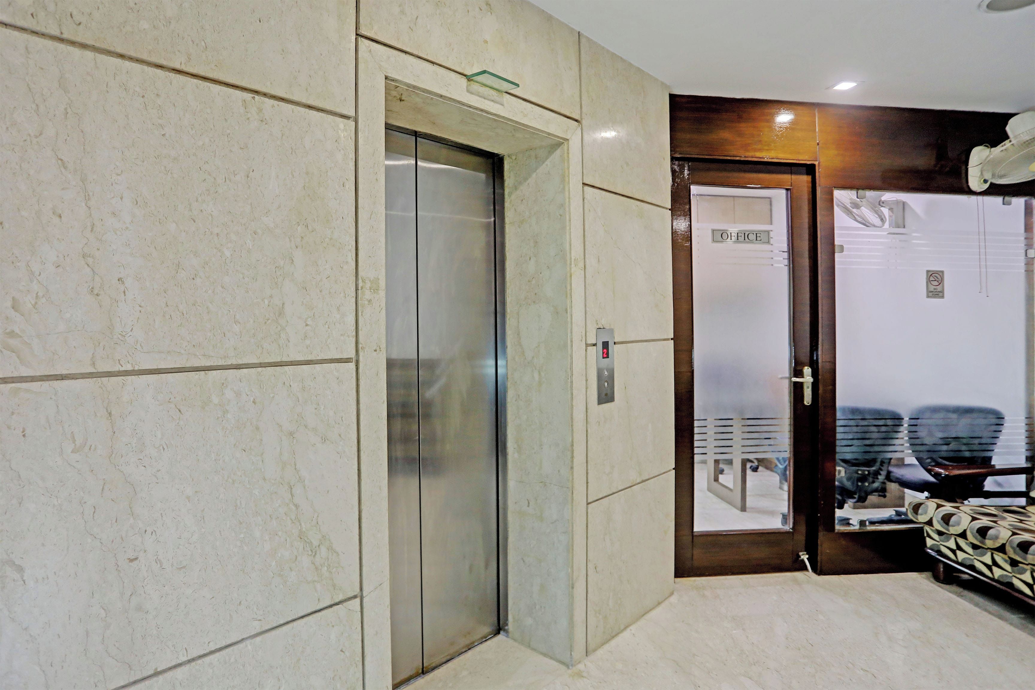 Vestíbulo de hotel con piso de mármol, un ascensor de vidrio y una mesa de recepción.
