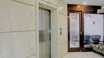 Vestíbulo de hotel con piso de mármol, un ascensor de vidrio y una mesa de recepción.