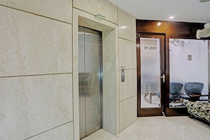 A hotel lobby with a marble floor, a glass elevator, and a reception desk. - Townhouse Relax Suits A Boutique (Ghaziabad)
