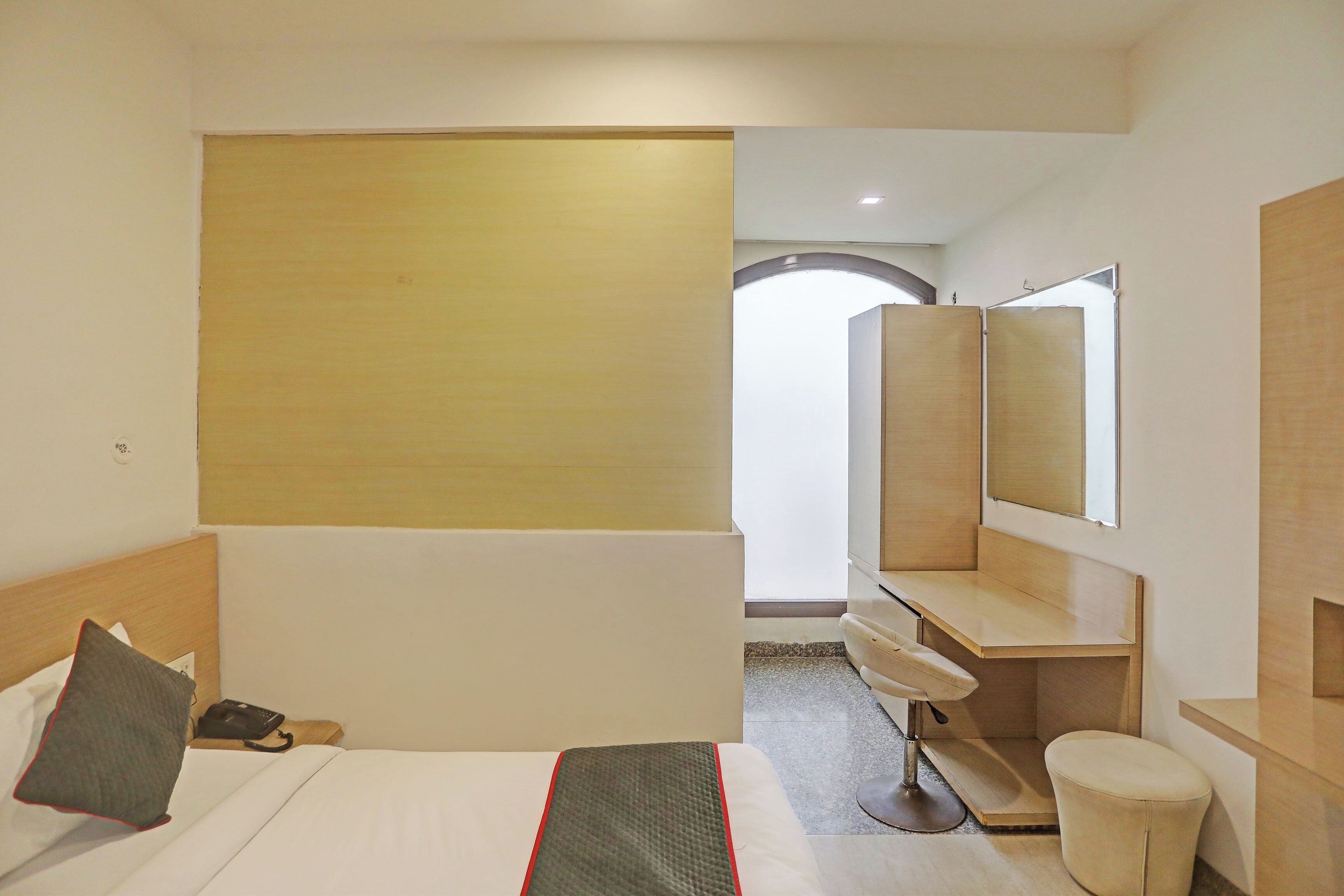 Habitación de hotel con cama, escritorio, silla, espejo y vistas al pasillo.