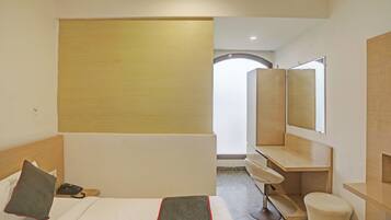 Habitación de hotel con cama, escritorio, silla, espejo y vistas al pasillo.