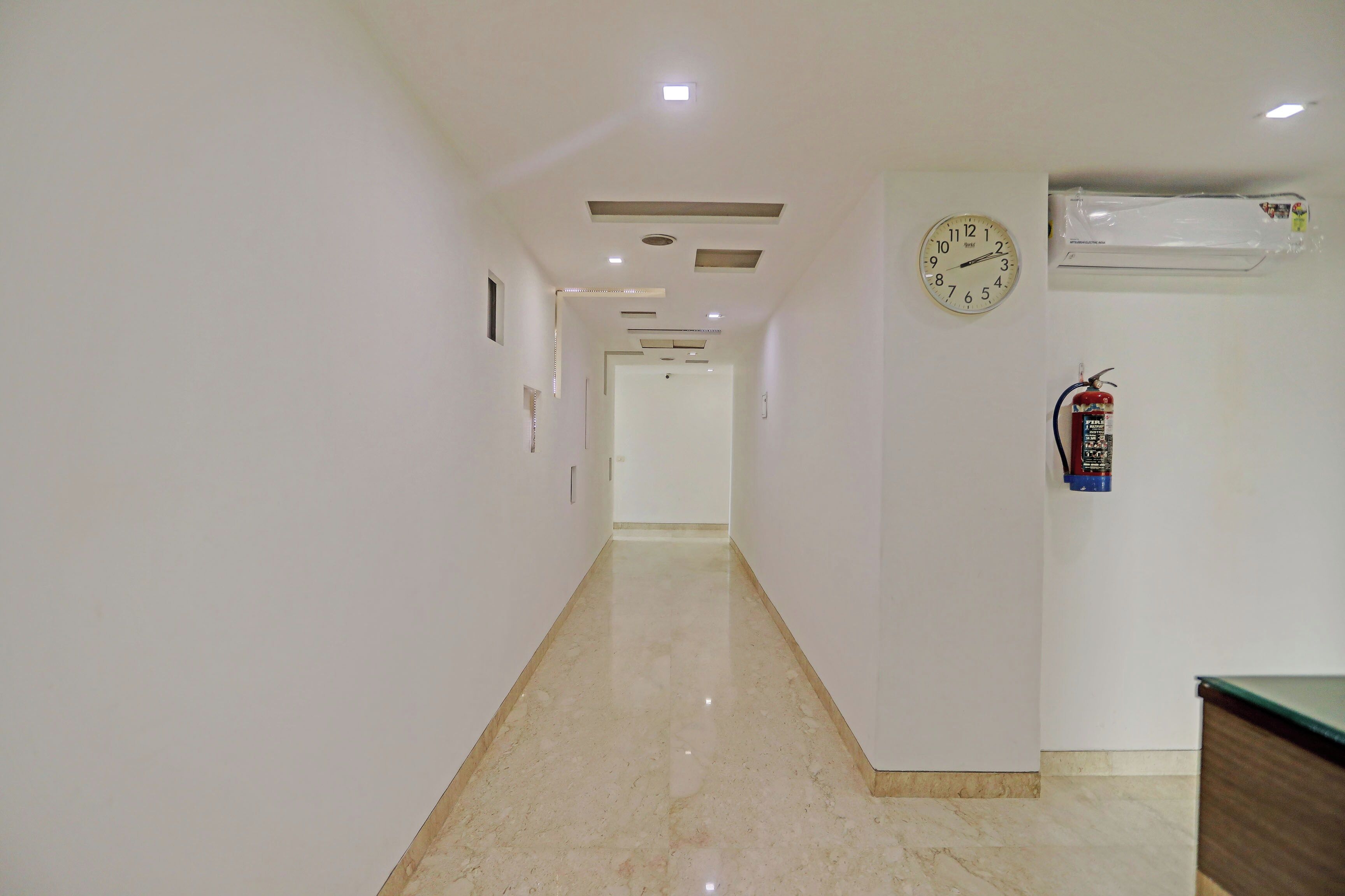 A hallway with a clock and a fire extinguisher on the wall.