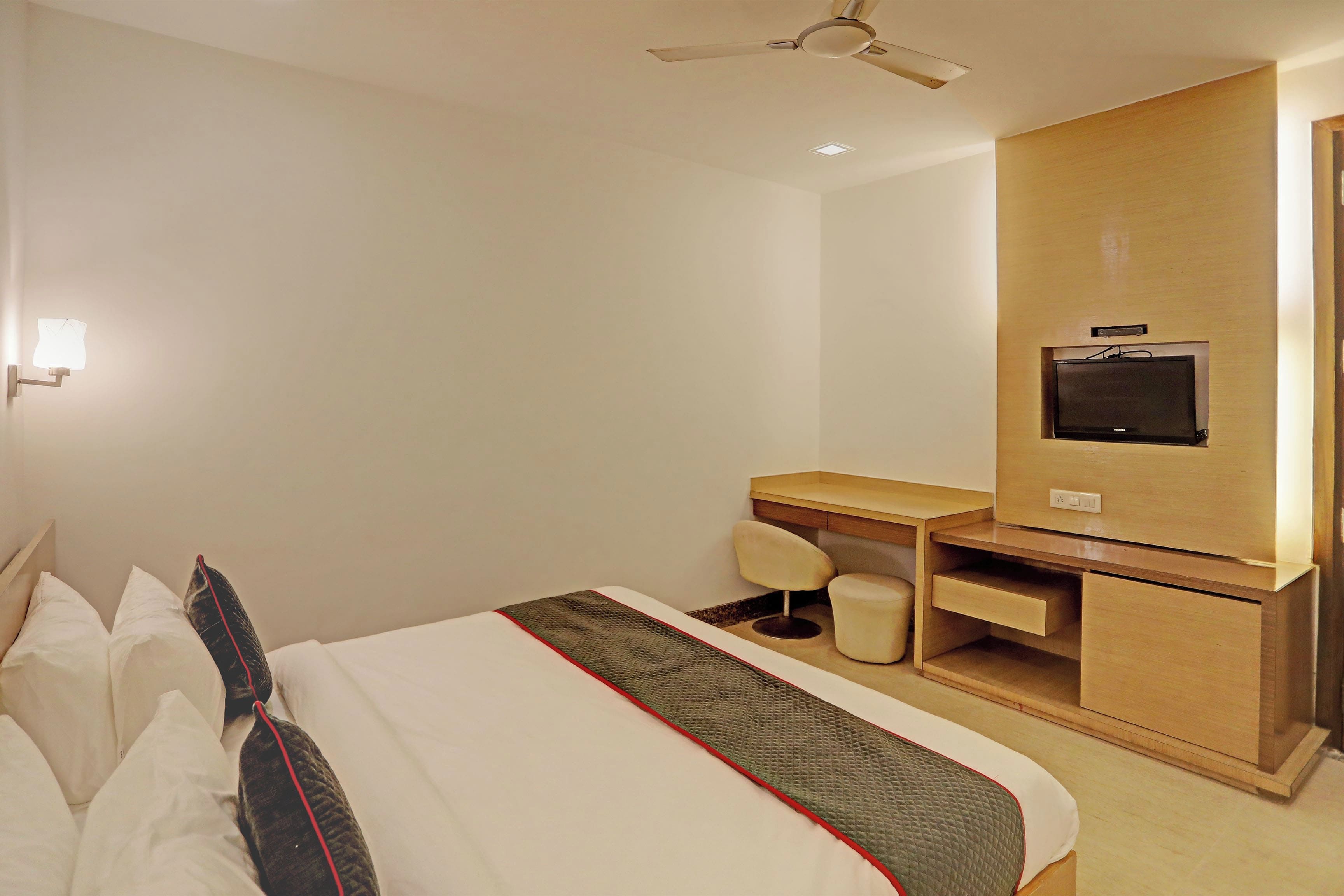 Ein Hotelzimmer mit Bett, Schreibtisch, Stuhl, Fernseher und Deckenventilator.
