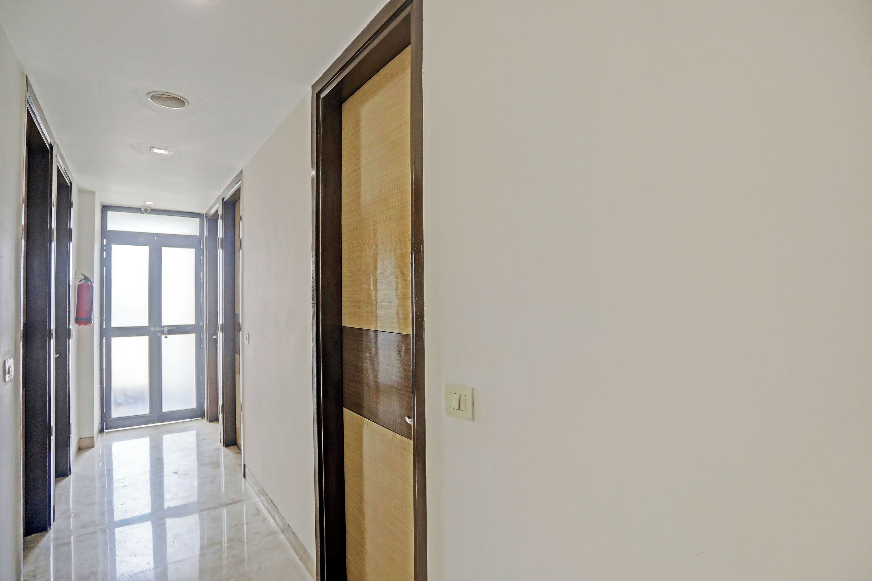Un pasillo con una puerta, un extintor y un interruptor de luz en la pared.
