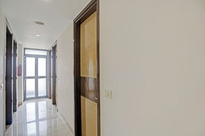 A hallway with a door, a fire extinguisher, and a light switch on the wall.