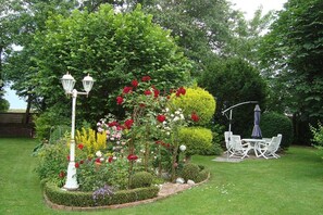 Een tuin vol verschillende bloemen, een witte lantaarnpaal en een tafel met stoelen.