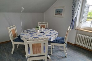 A dining area with a round table, white chairs with blue cushions, a white lamp, and a framed picture on the wall. - Holiday apartment with 2 bedrooms (Dornumersiel)
