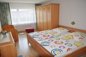 Ein Schlafzimmer mit einem hölzernen Bett, einem Holzschrank, einem roten Sessel und einem kleinen Tisch mit einer Vase.