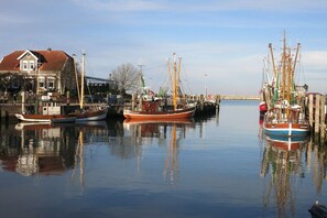Ein Hafen mit mehreren vertäuten Booten, ein Gebäude mit rotem Dach und eine ruhige Wasseroberfläche, die die Boote reflektiert.