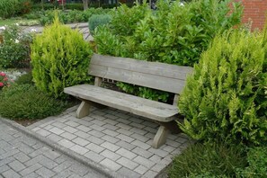 Eine hölzerne Bank in einem Garten mit grünen Sträuchern und einem Pflasterweg.