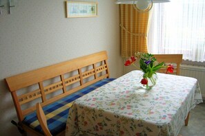 Ein Zimmer mit einer hölzernen Bank, einem Tisch mit einer blumigen Tischdecke und einer Vase mit Blumen.