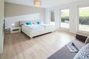 A modern bedroom with a large bed, bedside tables, and a view of the outdoors through large windows. - Holiday apartment in Juist with swimming pool (Juist)