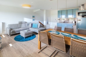 A modern living room with a sofa, ottoman, and dining table with chairs. - Holiday apartment in Juist with swimming pool (Juist)
