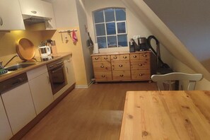 A kitchen with a wooden table, cabinets, a window, and a ceiling fan. - Holiday apartment in Föhr with 2 bedrooms (Nieblum)