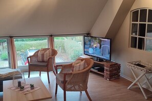 Una sala de estar acogedora con televisión, sillas de mimbre, una mesa de madera y vistas al exterior.