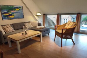 A modern living room with a sofa, a wooden coffee table, a wicker armchair, and a large window with curtains. - Holiday apartment in Föhr with 2 bedrooms (Nieblum)