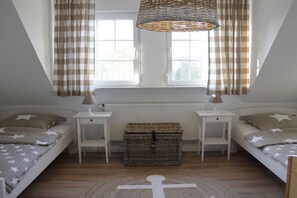 A bedroom with two beds, a wicker chest, a cross-shaped rug, and a window with curtains. - Holiday home in Dornum with swimming pool (Dornum)