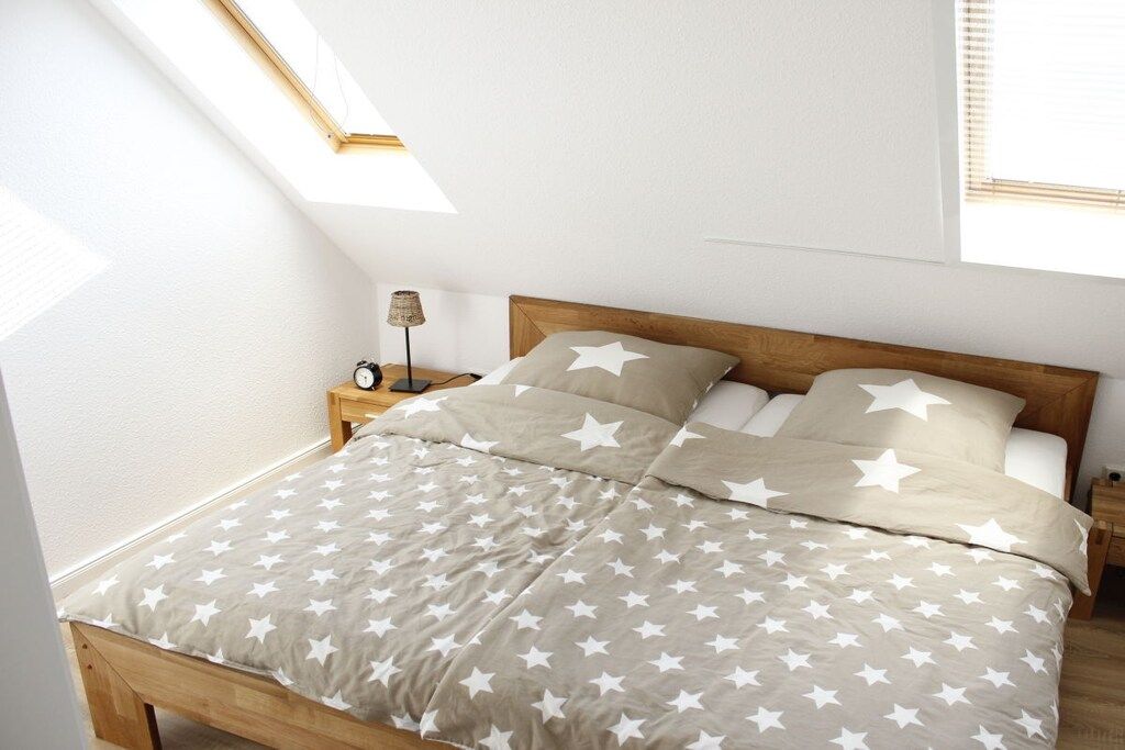 Una camera da letto con un letto, biancheria da letto a motivi stellati, un comodino con una lampada e una finestra con persiane.