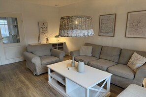 A modern living room with a white coffee table, two grey sofas, a wicker pendant light, and framed artwork on the walls. - Holiday home in Dornum with swimming pool (Dornum)