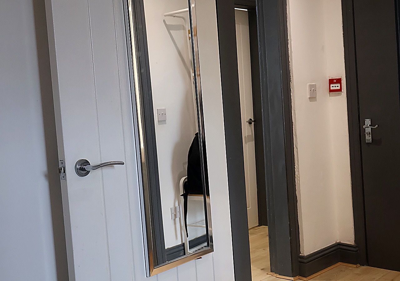 A hotel corridor with doors, a mirror, and a red emergency light switch.