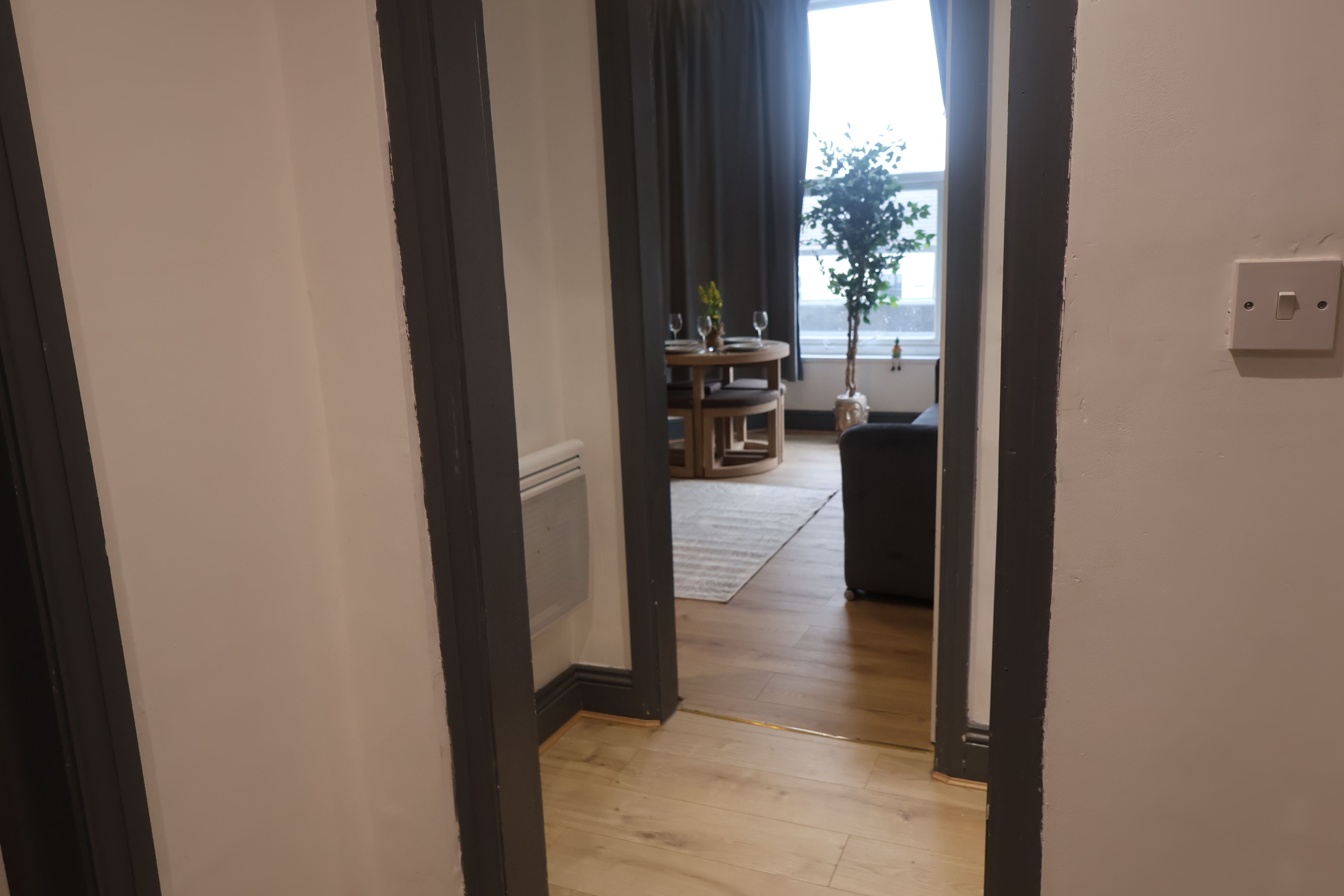 A hallway leading to a dining area with a table and chairs, a potted plant, and a window with a view.