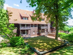 A multi-story building with a sloped roof, balconies, and a garden area. - Holiday Apartment With 3 Bedrooms (Braunlage)