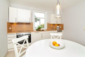 A modern kitchen with white cabinetry, a wooden countertop, and a dining table with a fruit bowl. - Holiday apartment with 1 bedroom (Wittdün)