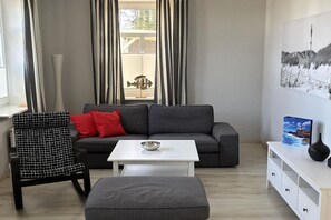 A modern living room with a grey sofa, a black and white checkered chair, a white coffee table, and a white cabinet with drawers. - Holiday apartment with 1 bedroom (Wittdün)