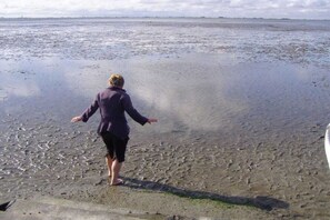 Eine Person steht auf einem nassen Strand, im Hintergrund ist ein Gewässer zu sehen.