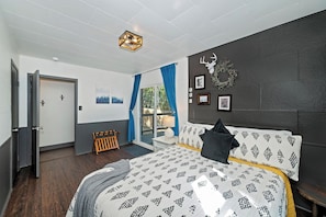 A bedroom with a bed, a headboard, a wall-mounted light fixture, a door, and a window with curtains. - PET FRIENDLY Boulder Bay Retreat with HOT TUB Under the Pines, Remodeled Kitchen, Multiple Decks, Outdoor Games & Cozy Mountain Charm! (Big Bear Lake)