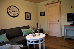 Ein Wohnzimmer mit einer Couch, einem runden Tisch mit Kerzen, einer Uhr und einem Fernseher.