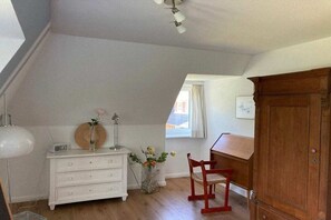A room with a sloped ceiling, a white dresser, a wooden chair, a cabinet, and a window with curtains. - Holiday home in Nebel with swimming pool (Nebel)