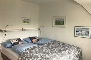 A single bed with a patterned bedspread, two wall-mounted lamps, and two framed landscape paintings. - Holiday home in Nebel with swimming pool (Nebel)
