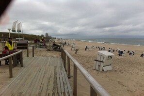Ein Strand mit einer Holzpromenade, Liegestühlen und einem Rettungsschwimmerstand.