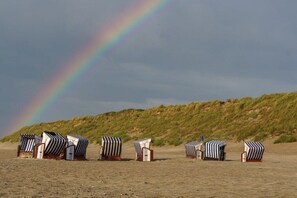 Beach huts with striped awnings, a clear sky, and a distant dune. - House Hahnen - Ground Floor (Norderney)