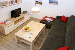 Ein modernes Wohnzimmer mit einer Couch, einem Couchtisch mit einer Fruchtschale, einem Fernseher und einem Bücherregal.