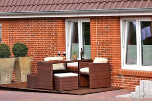 Ein Backsteinhaus mit einer Terrassenfläche, die Korbmöbel und Kübelpflanzen zeigt.