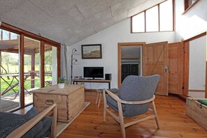 Ein Zimmer mit Holzboden, einem Fernseher auf einem Schrank, einem Sessel und einem Tisch.