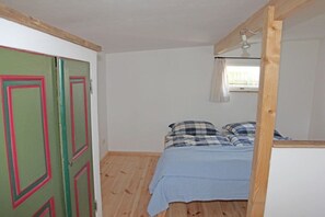 Ein Schlafzimmer mit einem Bett, Holzboden, einer grünen Tür mit rotem Zierstreifen und einem Fenster mit Vorhängen.