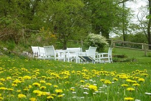 Buiten zitplaatsen met witte stoelen en tafels, omringd door een gazon met gele bloemen.
