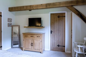 A bedroom with a wooden ceiling, a television on a shelf, a wooden cabinet, a door with a black handle, and a white chair. - Willow Tree Barn (Bideford)