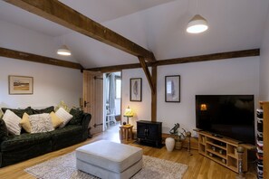 A spacious living room with a large television, wooden beams, a sofa, and a fireplace. - Willow Tree Barn (Bideford)