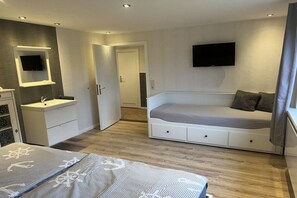 A modern bedroom with a bed, a built-in bench, a TV mounted on the wall, and a door leading to another room. - Holiday apartment with 1 bedroom (Tönning)