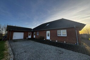 A two-story house with a garage, a front porch, and a gravel driveway. - Holiday home in the North Sea with 2 bedrooms (Westerhever)